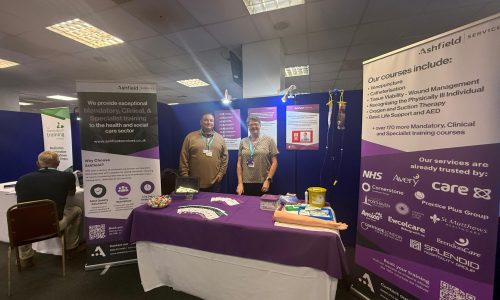 Billy and Paula on the Stand Billy and Paula from Ashfield Services standing at their exhibition stand during the Sussex Care Showcase 2025, displaying information about mandatory, clinical, and specialist training courses for the health and social care sector.